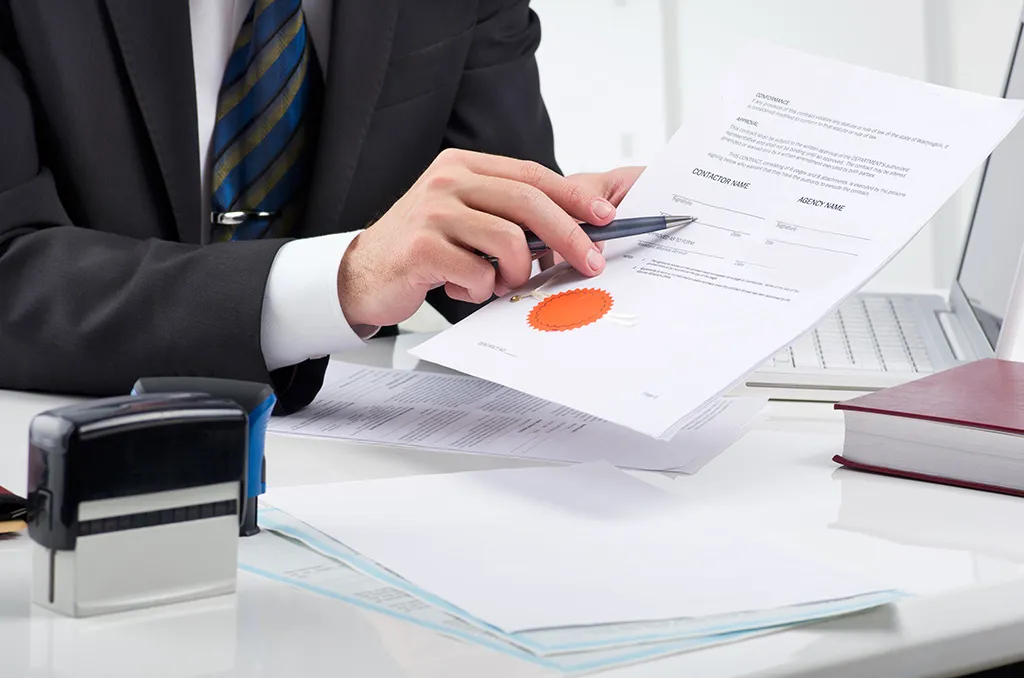 A businessman checking a certified document beside a company stamp at his desk